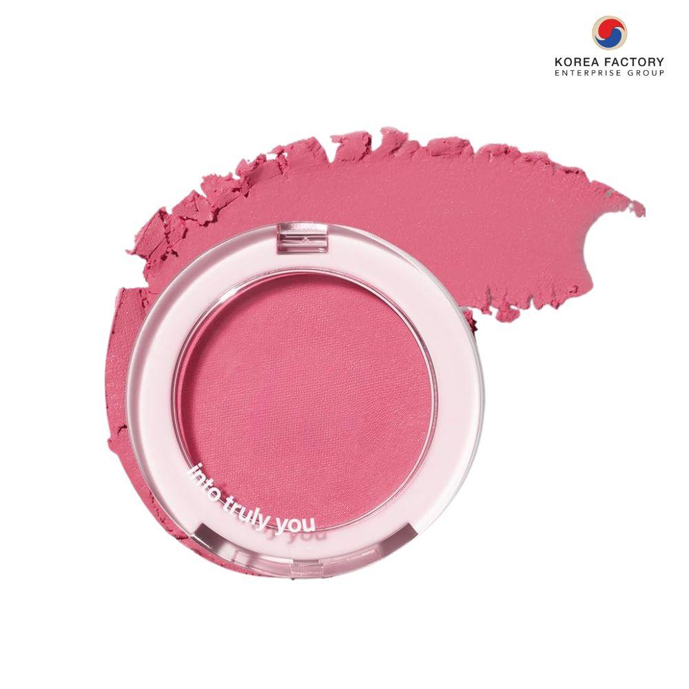 บลัชออนสีชมพูในตลับใสฝาใส วางบนสวอชบลัชที่ปาดเป็นครึ่งวงโค้งบนพื้นขาว พร้อมโลโก้ Korea Factory Enterprise Group