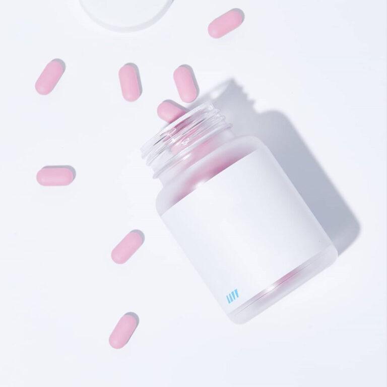 มือกำลังจับขวดอาหารเสริมแบบแคปซูลสีขาวบนแผ่นไม้และผ้าซาติน